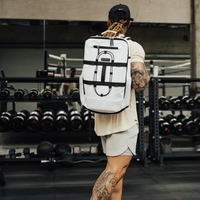 Blizzard White Ai1 gym backpack worn on both shoulders beside a dumbbell rack