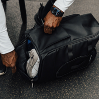 Hands unzipping the separate shoe compartment of a black Ai1 gym backpack, sneakers tucked inside