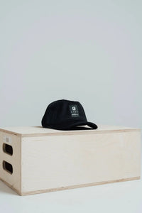 Midnight Black mesh golf hat with a Give Your All patch, resting on a wooden box