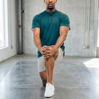 Man kneeling in a lunge wearing Ghost Grey 6 inch golf shorts and a teal henley
