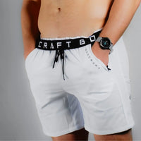 Close front view of white training shorts, BodCraft waistband text visible, smartwatch on wrist