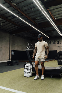 Man in cream training gear beside a treadmill, Blizzard White Ai1 backpack on the turf