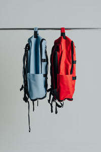 Red and light blue Ai1 gym backpacks hanging side by side, seen from the side