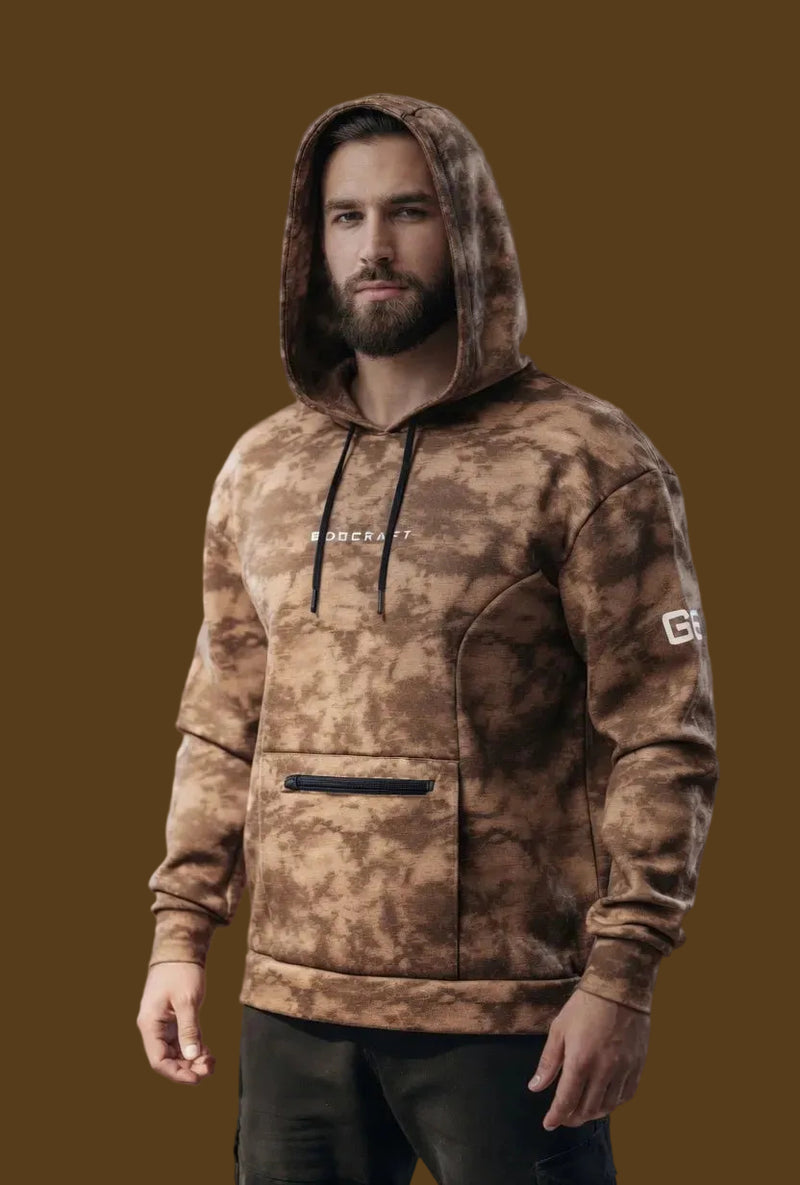 Man wearing a camouflage hoodie with visible branding against a neutral background