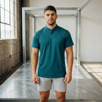 Ghost Grey golf shorts worn with a teal henley golf shirt, front view in a steel-frame studio