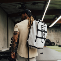 Man in a cream tee wearing the Blizzard White Ai1 backpack over one shoulder in a gym