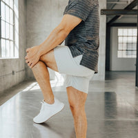 Man stretching one knee to his chest in Pebble Grey 6 inch golf shorts, showing the stretch leg opening