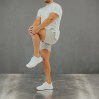 Ghost Grey golf shorts during a knee-to-chest stretch, white tee, grey studio backdrop