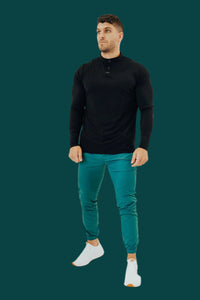 Man in a black henley and Pine Green golf joggers on a teal backdrop