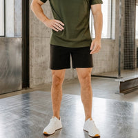 Midnight Black 6 inch inseam golf shorts from the waist down, hand on hip, white trainers