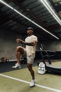 Athlete doing a high-knee drill on gym turf with the white Ai1 backpack on the floor behind
