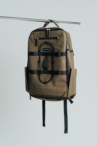Olive Ai1 gym backpack hanging from a rail, front view with bungee cord and compression straps