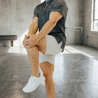 Pebble Grey golf shorts during a standing knee hug stretch, grey tee, sunlit studio