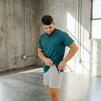 Man adjusting the waistband of Ghost Grey 6 inch golf shorts, teal short sleeve shirt