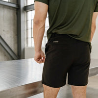 Close-up of the back pocket on Midnight Black 6 inch inseam golf shorts, worn with an olive tee