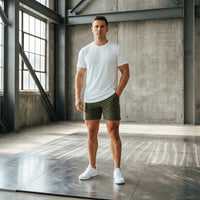 Full-length shot of Dark Olive men's golf shorts with a white tee, standing by tall factory windows